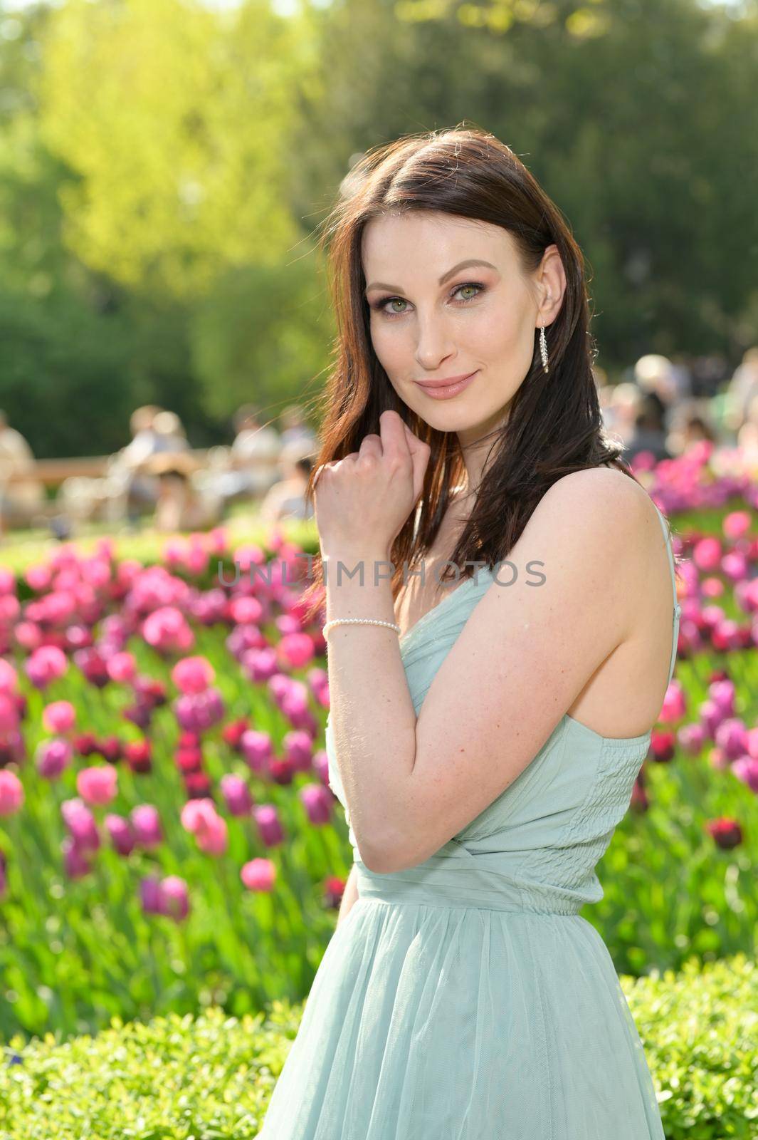A beautiful young Russian woman in a park in the first warm spring sun with a light turquoise dress.