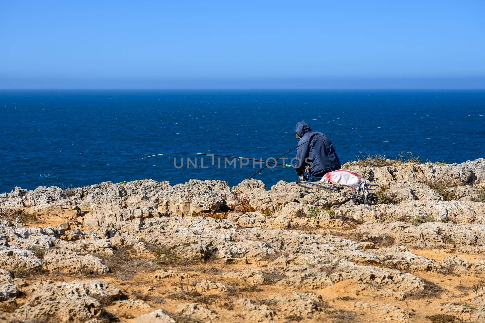 A lonesome fisherman is is sitting on the rocks and is catching his dinner with an huge fishing rod.