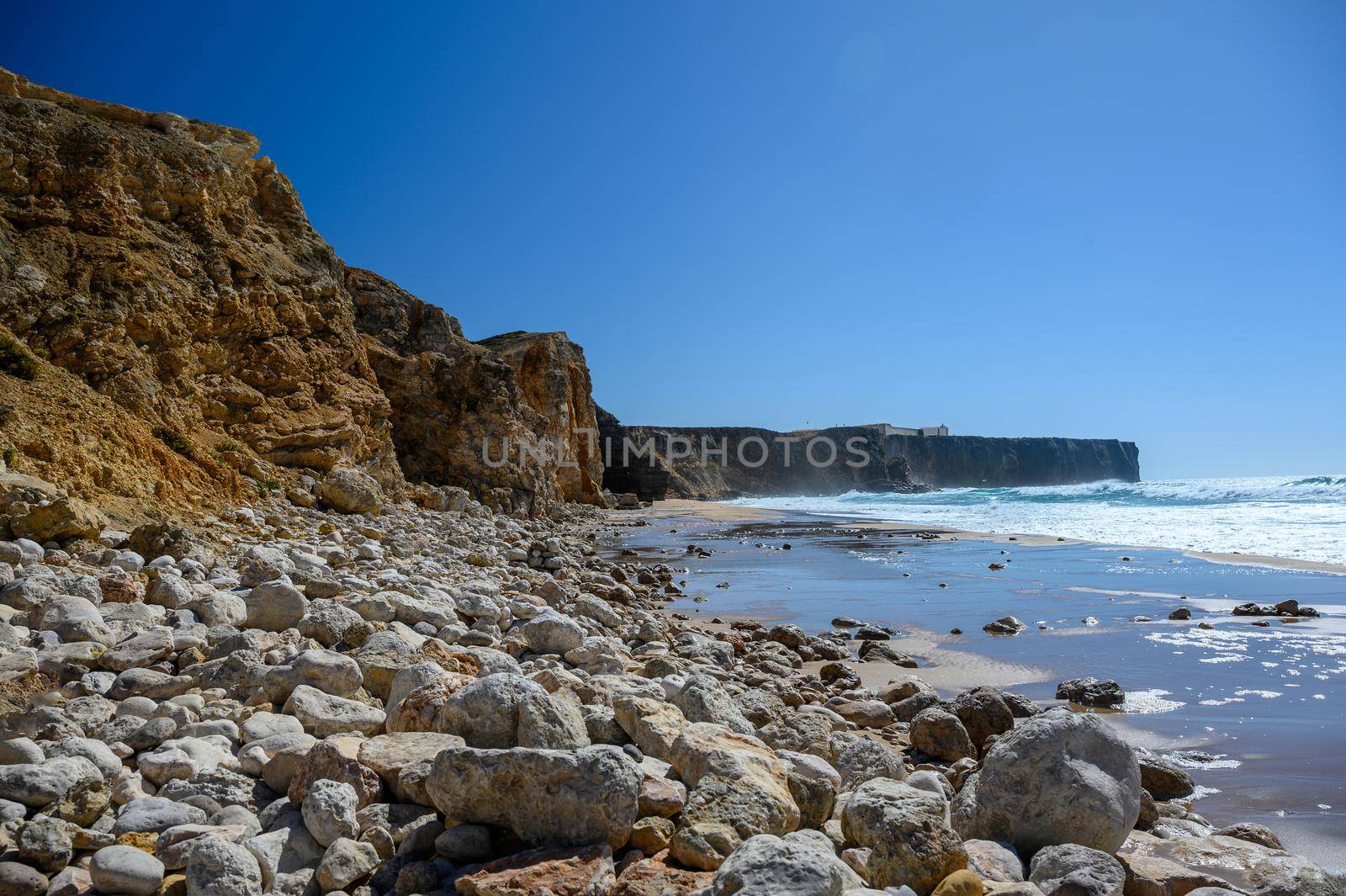 A beach with high rough cliffs at the Algarve in Portugal with some powerful waves.