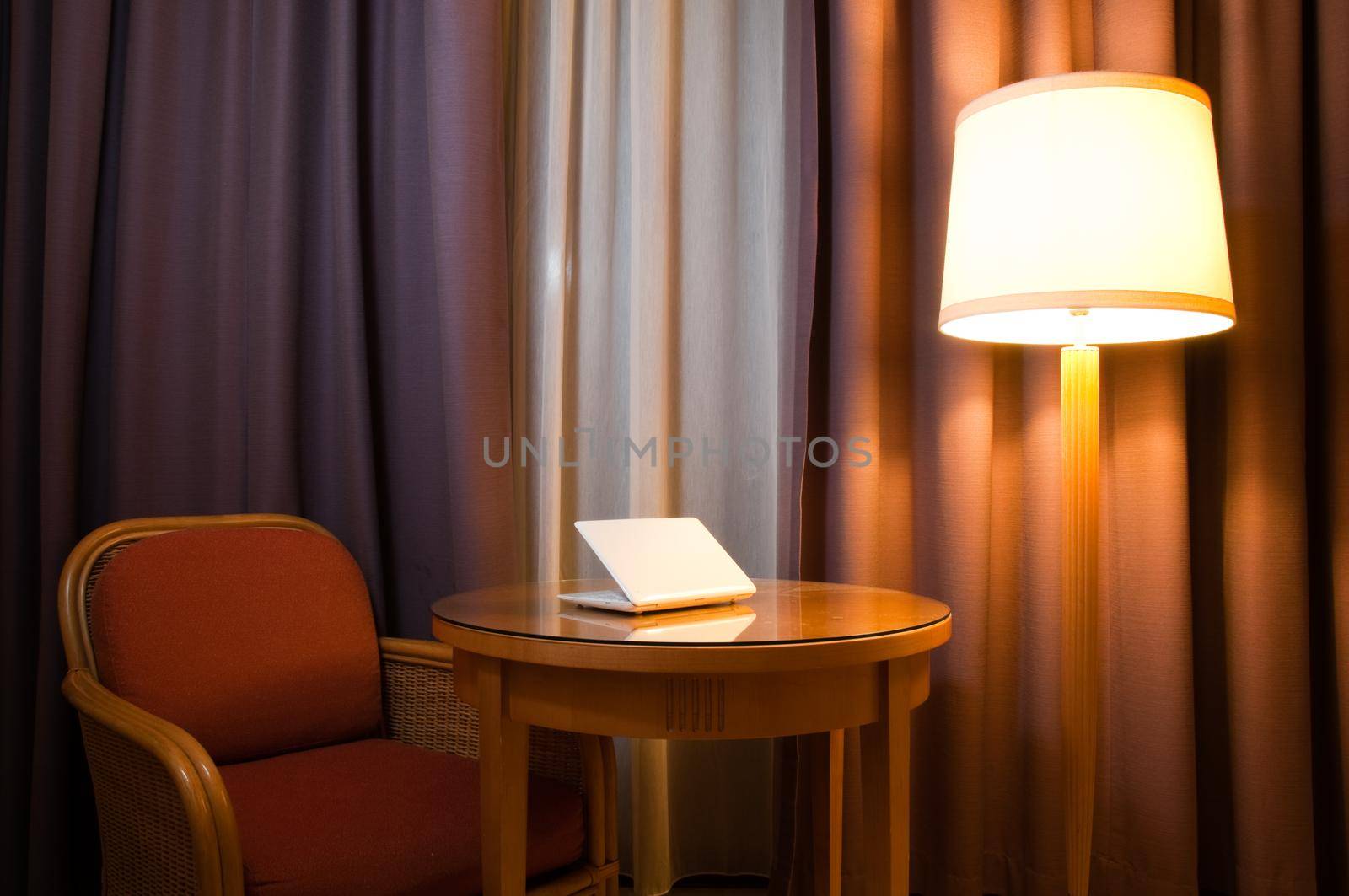 notebook computer on the table in the room with lamp, chair and curtains on the window