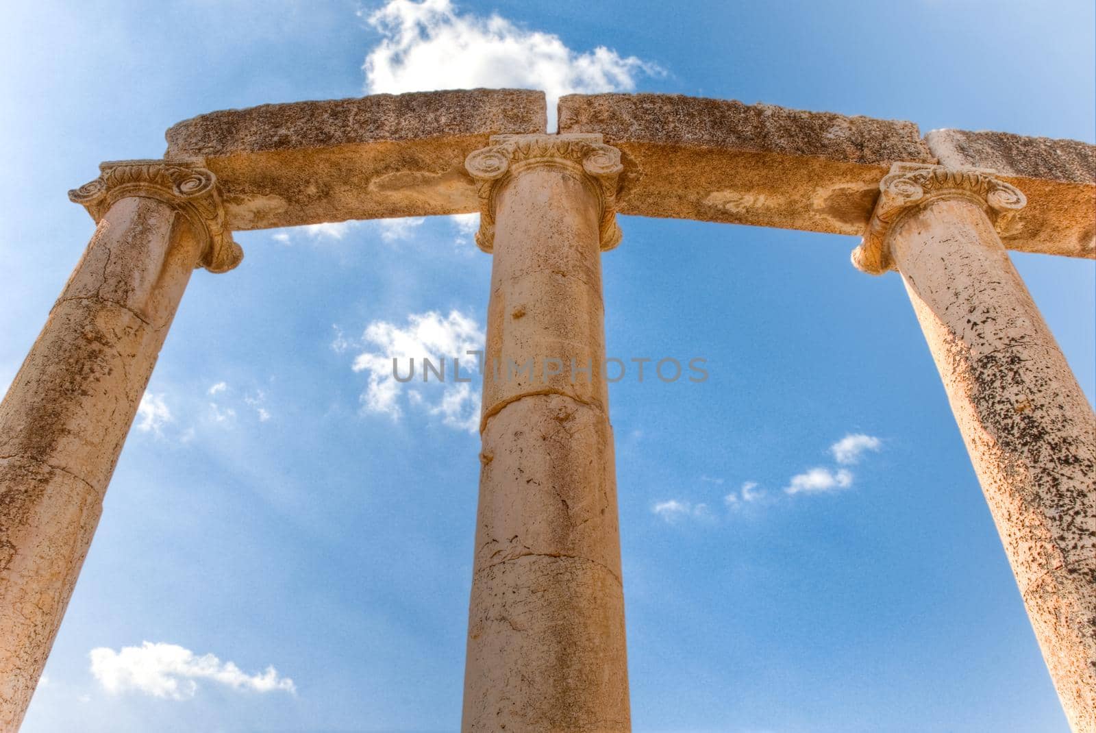 ancient roman columns against blue sky background with white clouds