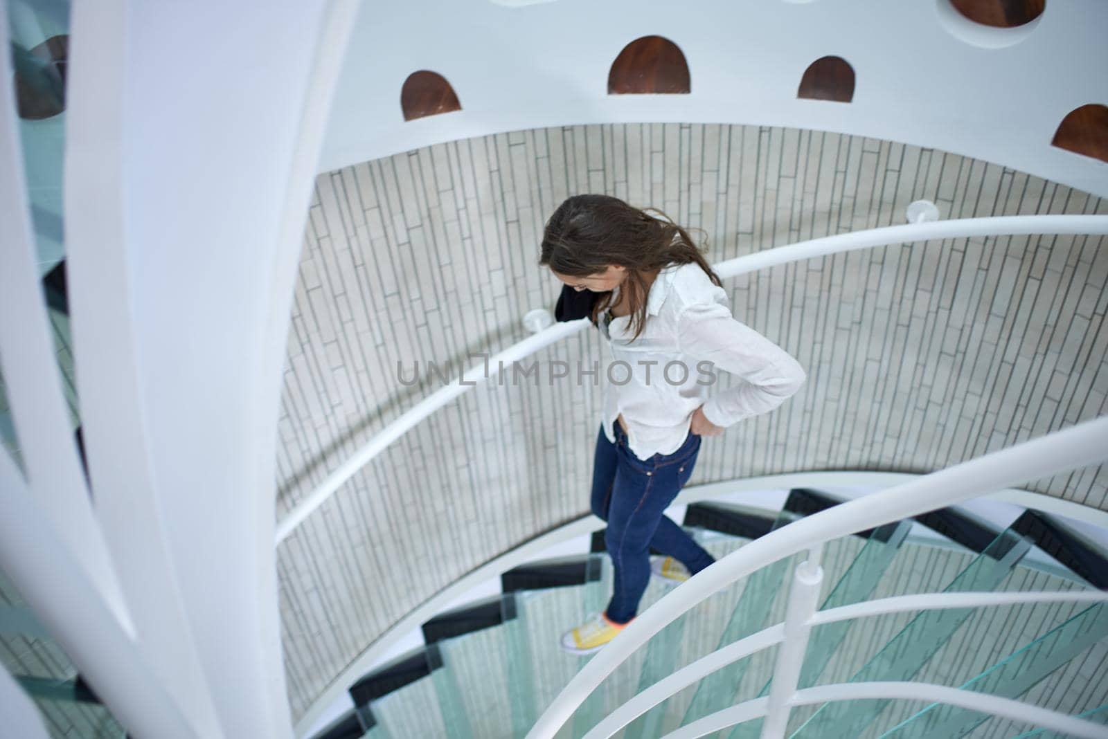 young woman walking on spiral stairs in modern home indoors