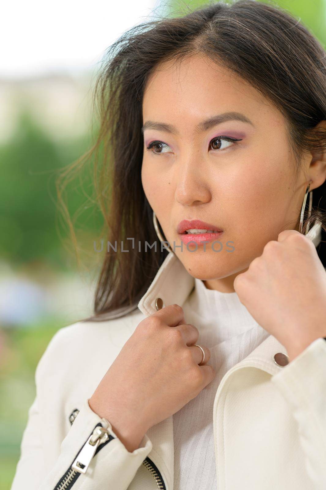 A young pretty Mongolian woman with a white leather jacket
in an urban park.