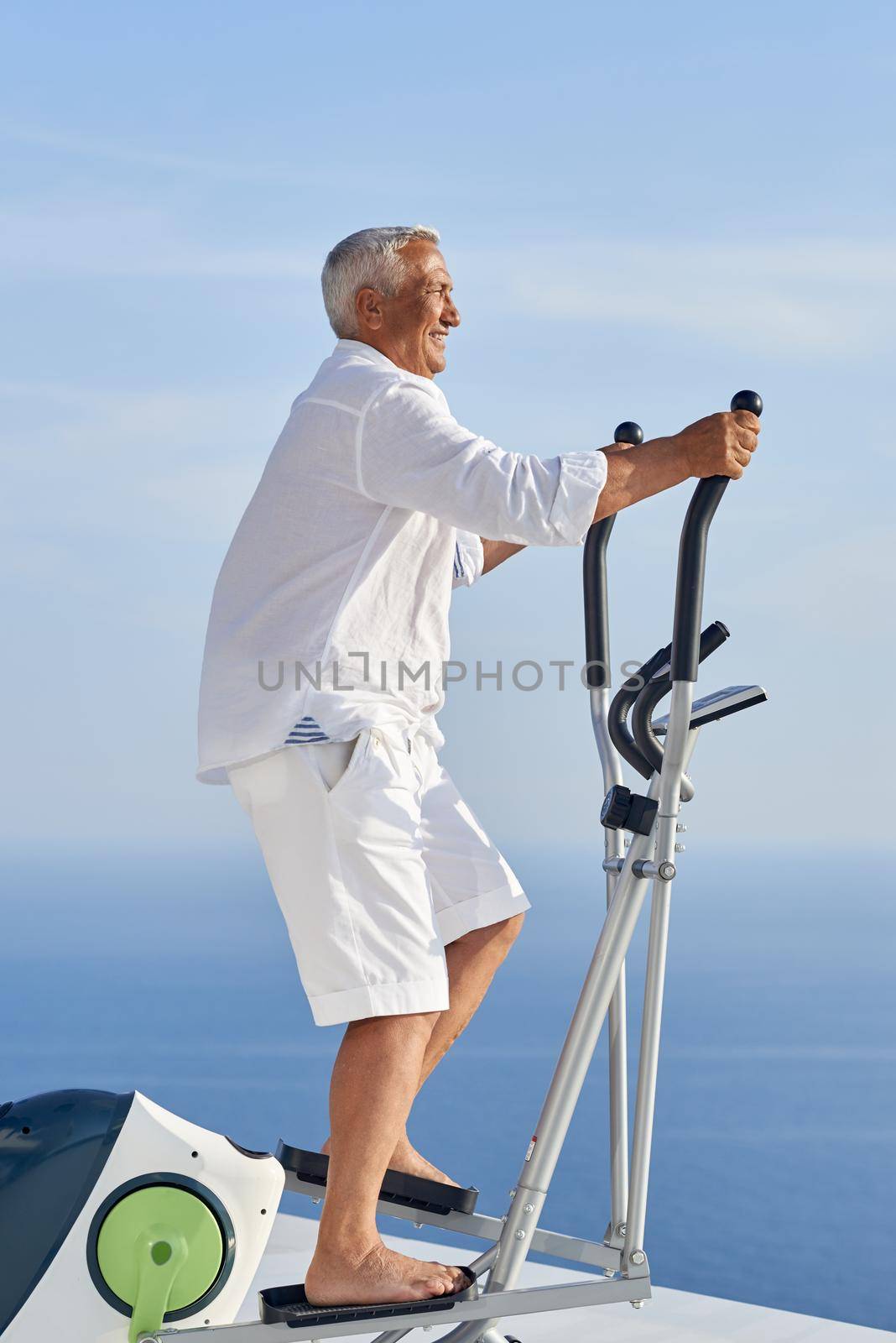 healthy senior man working out on gym treadmill machine at modern home terace with ocean view