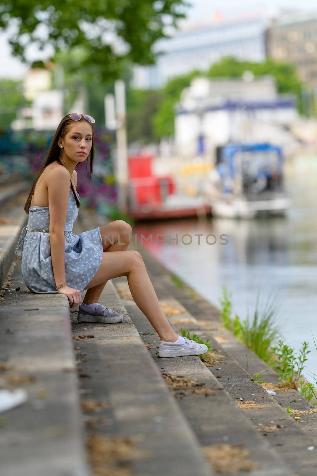 A portrait of a pretty young woman taken in the summertime in a city sitting on a staircase next to a river.