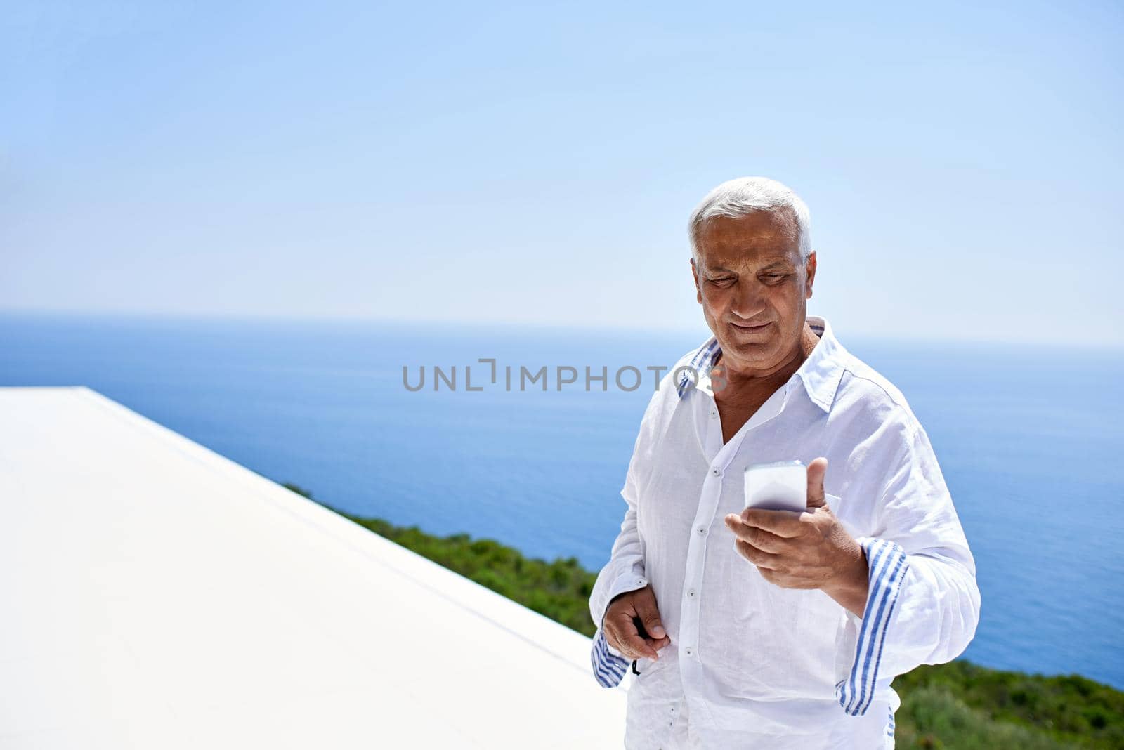 senior man using smart phone outdoor with ocean view background