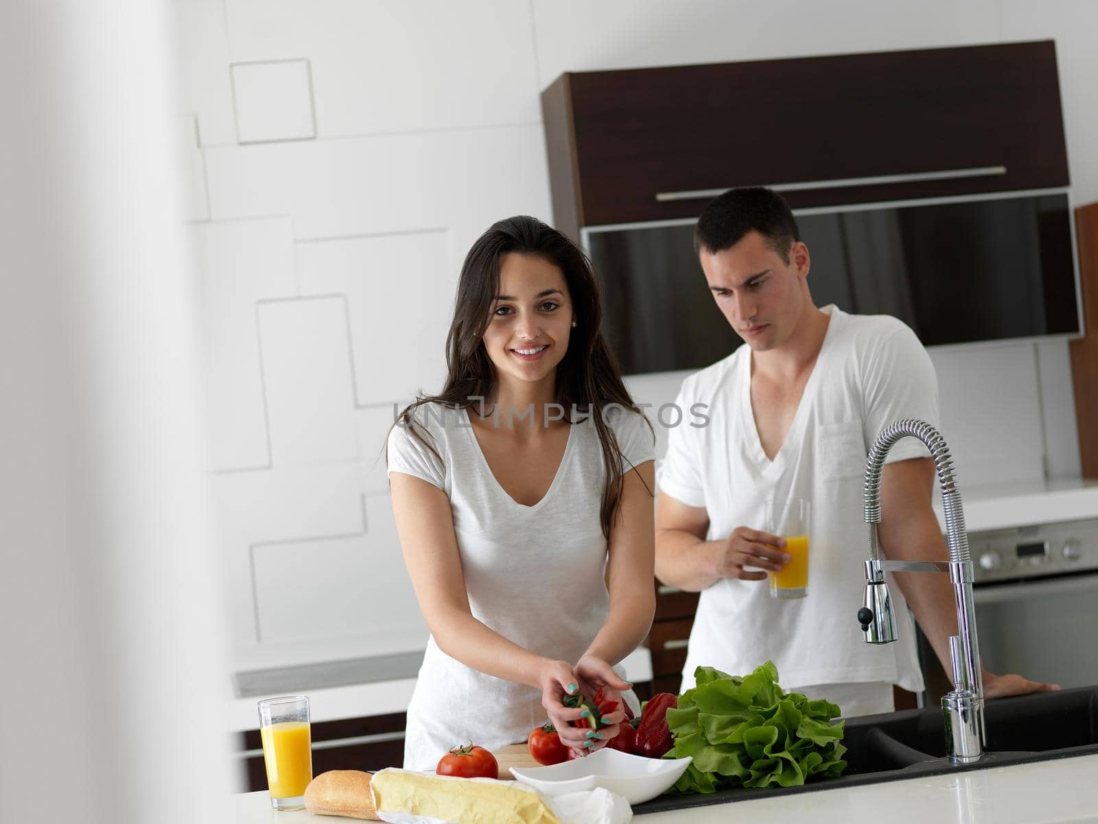 happy young couple have fun in modern kitchen indoor while preparing fresh fruits and vegetables food salad