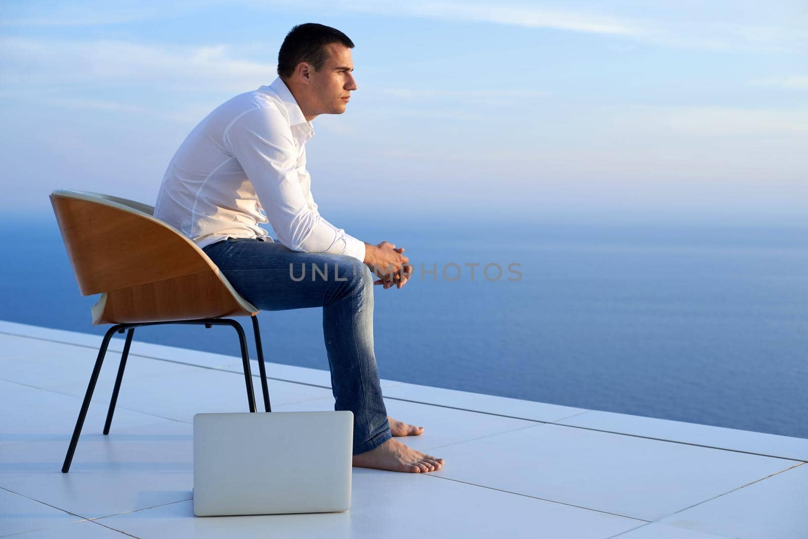 handsome young man relaxing and working on laptop computer at home balcony while looking sunset