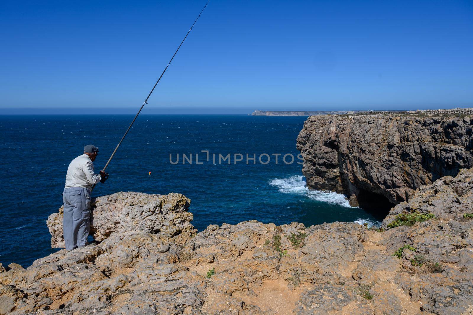 A lonesome old fisherman is catching his dinner with an huge fishing rod.