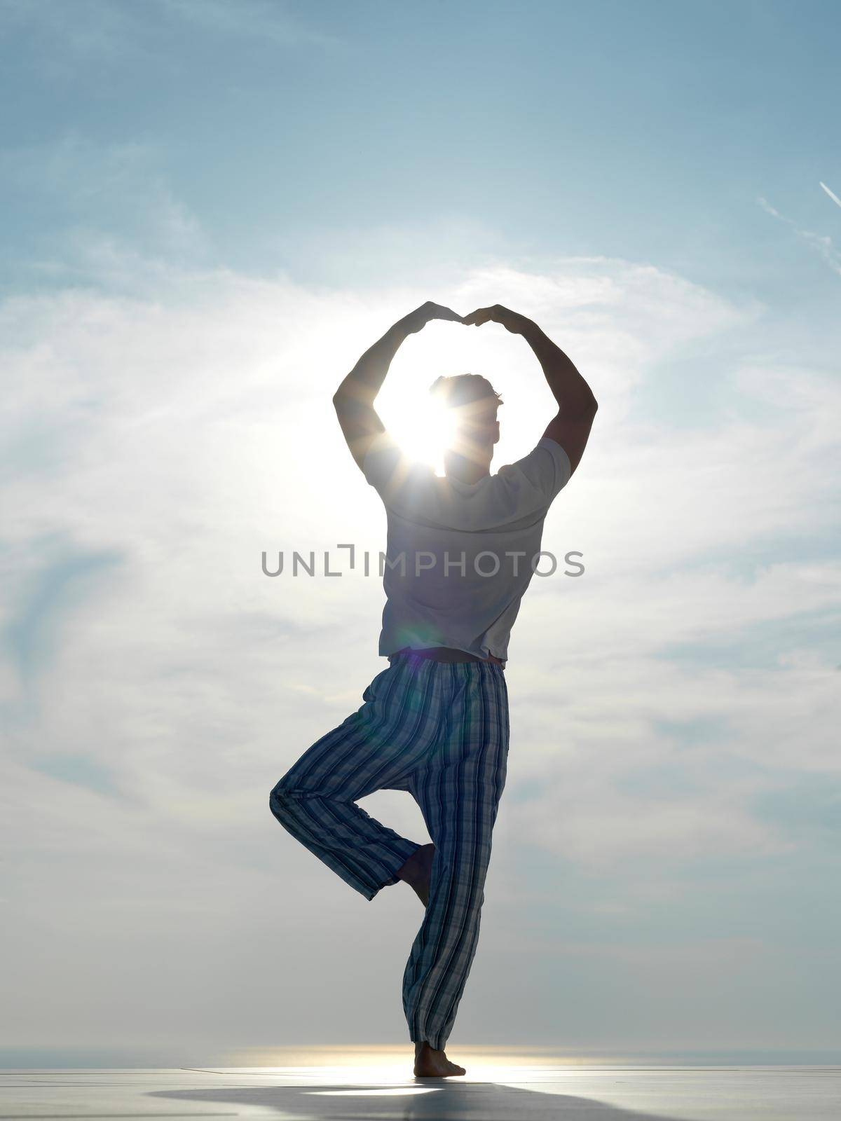 handsome young man practicing yoga on in modern home terace with ocean and sunset in background