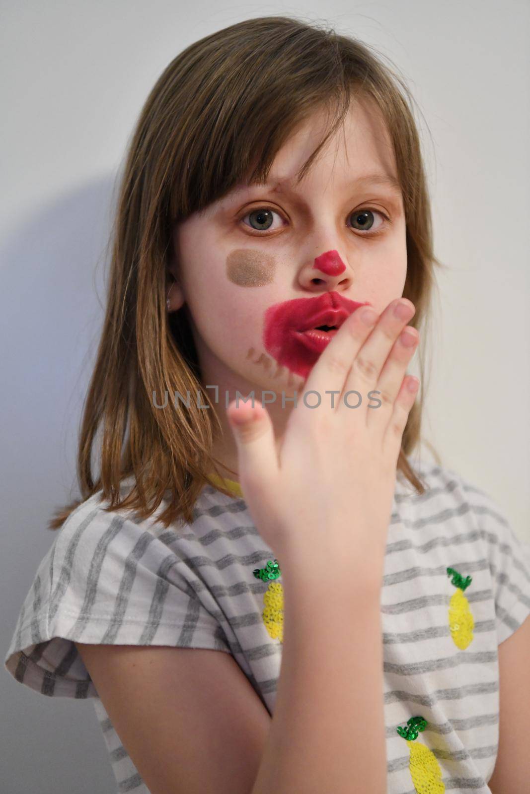 Cute little preschool girl playing with mommy's make up. Fashion experiment little child applying makeup lipstick and shadow on face, staying at home in corona virus quarantine.