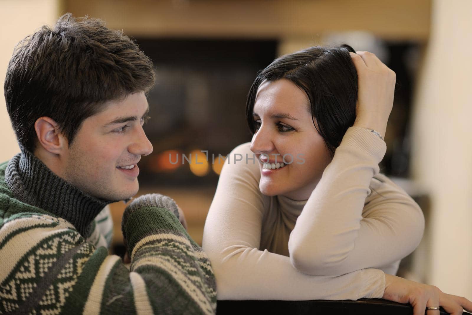 Young romantic couple sitting on sofa in front of fireplace at home by dotshock