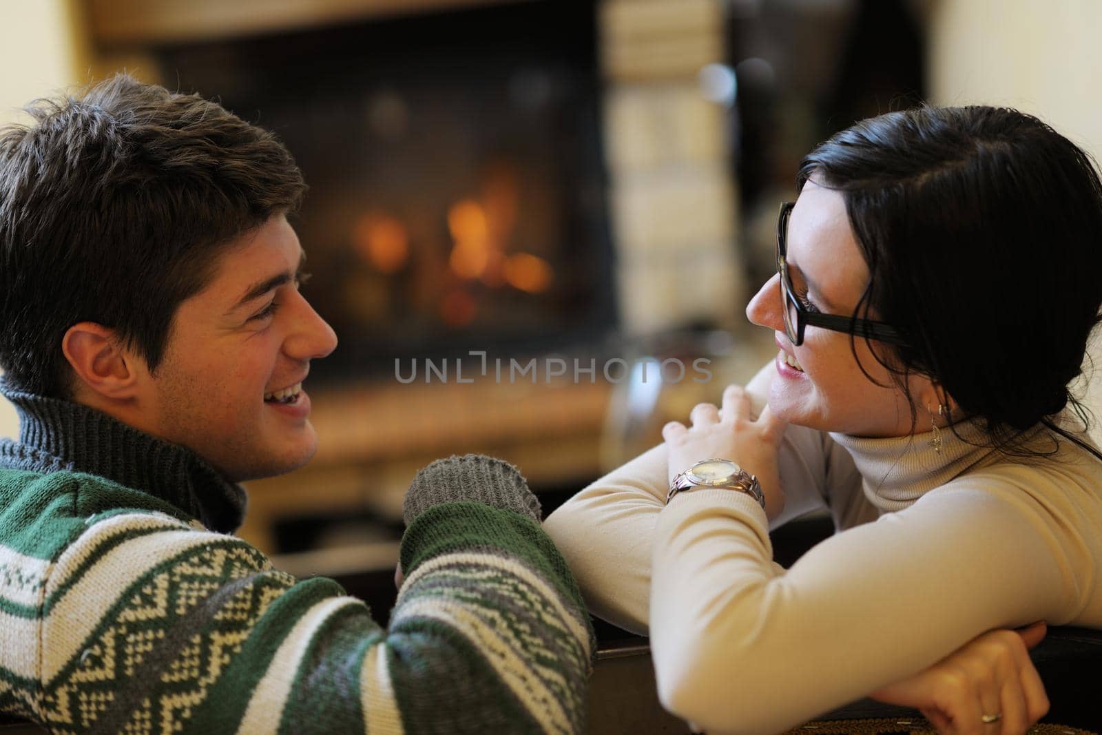 Young romantic couple sitting on sofa in front of fireplace at home by dotshock