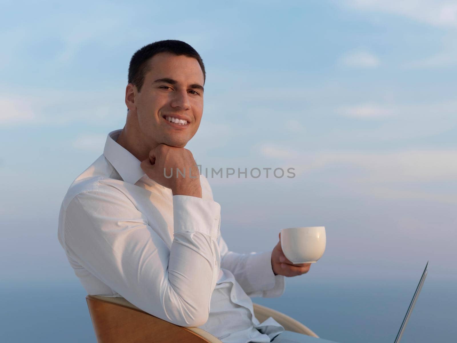 handsome young man relaxing and working on laptop computer at home balcony while looking sunset