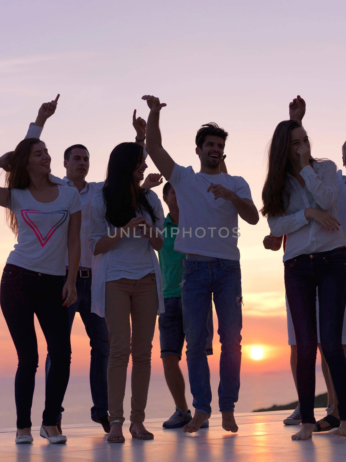 group of happy young people dancing and have fun on party in modern home bacony with sunset and ocean in background