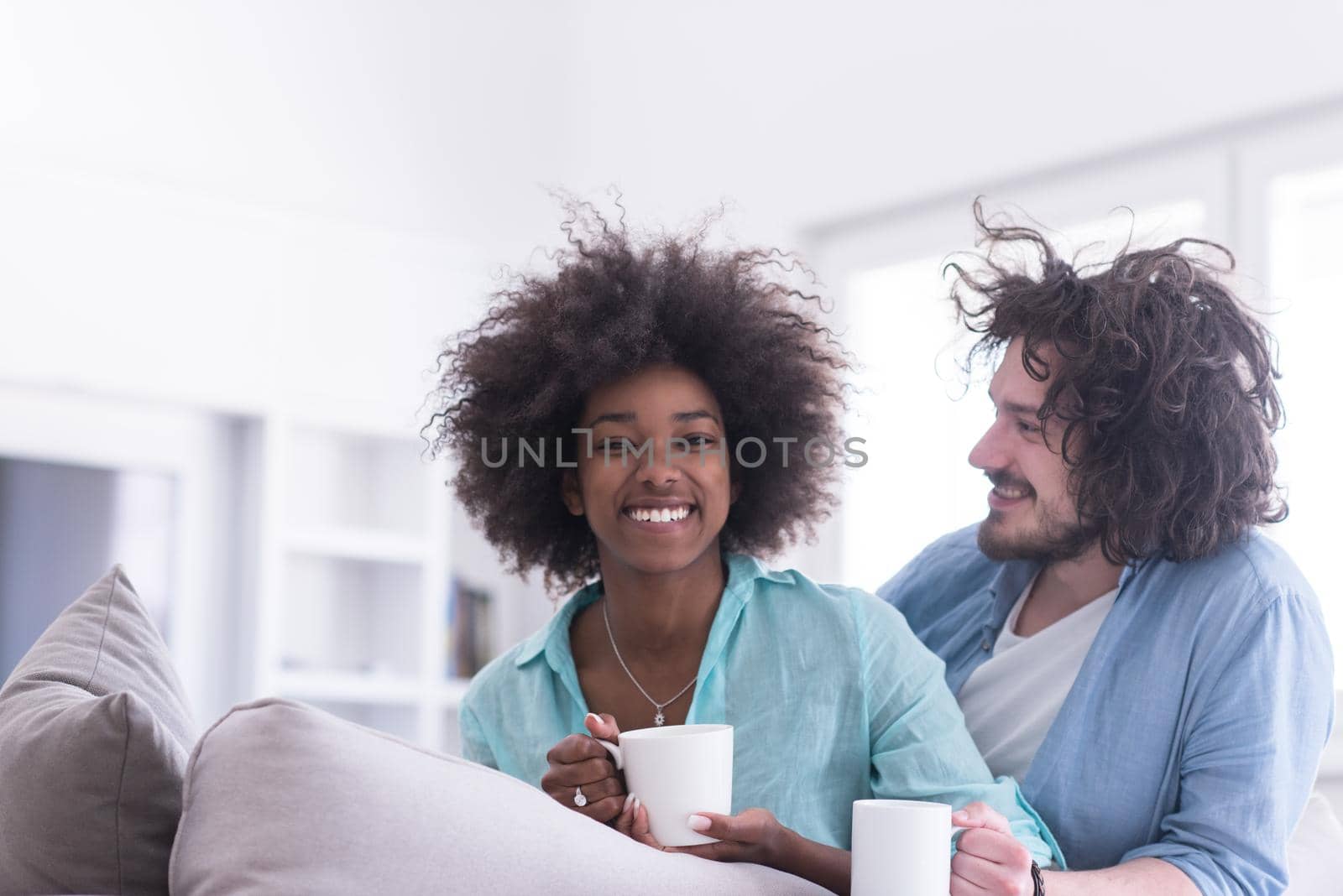 multiethnic couple sitting on sofa at home drinking coffe by dotshock