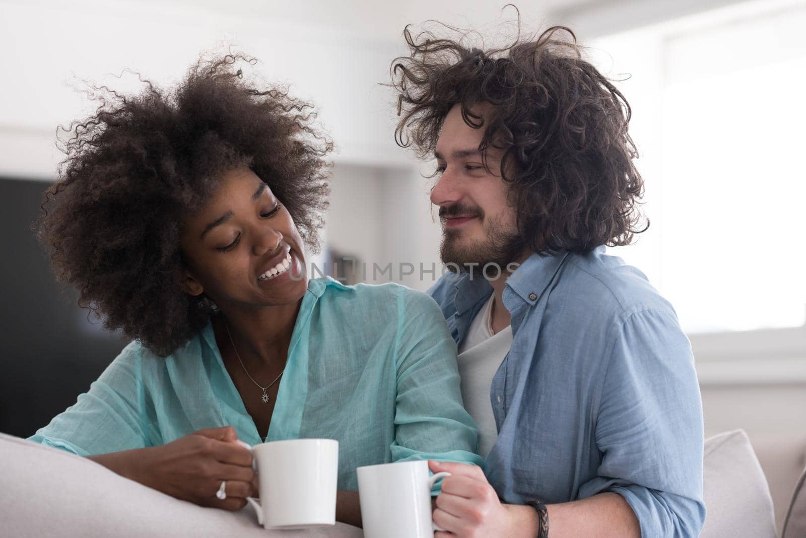 multiethnic couple sitting on sofa at home drinking coffe by dotshock