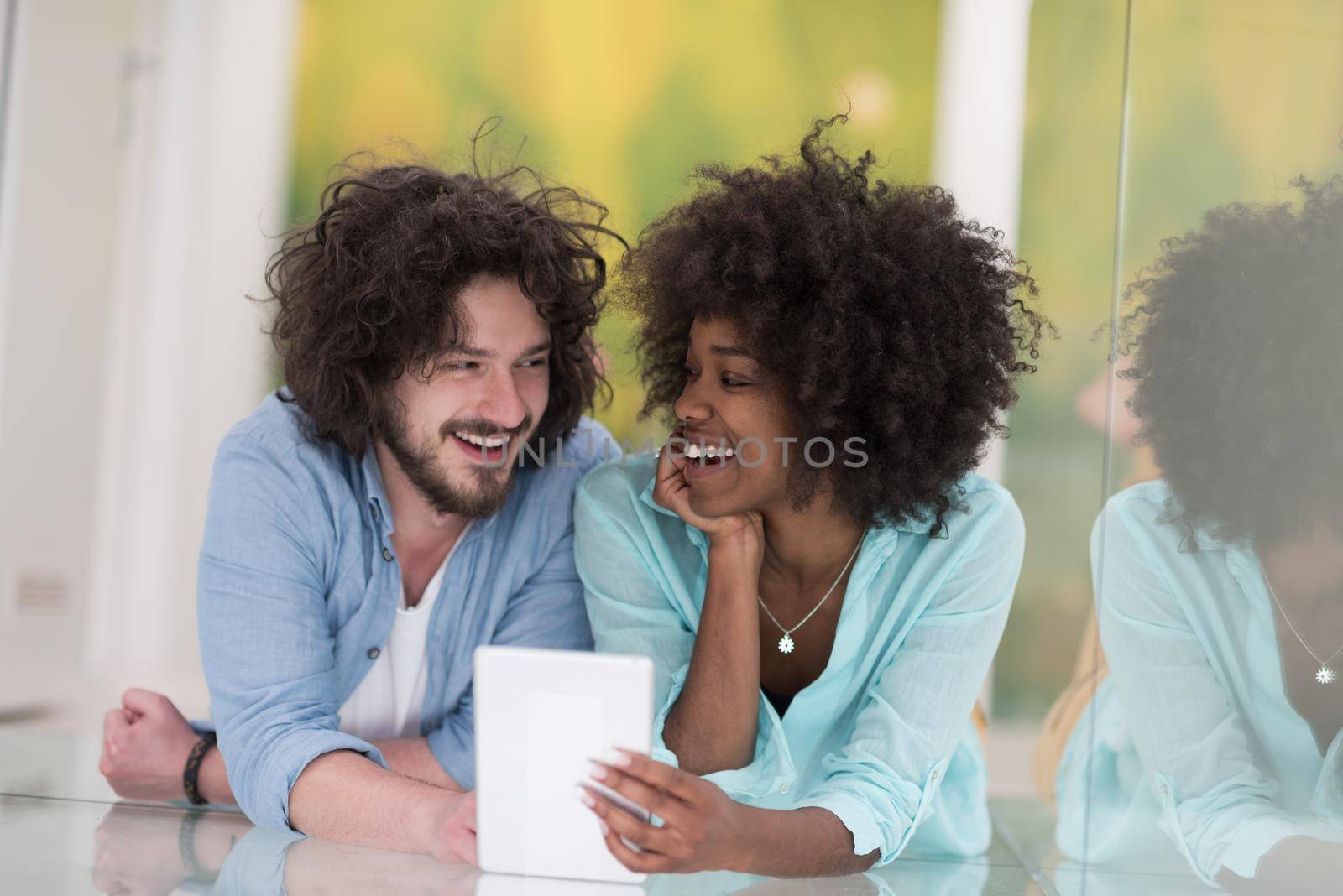 Happy young multiethnic couple lying on floor having fun using Digital Tablet