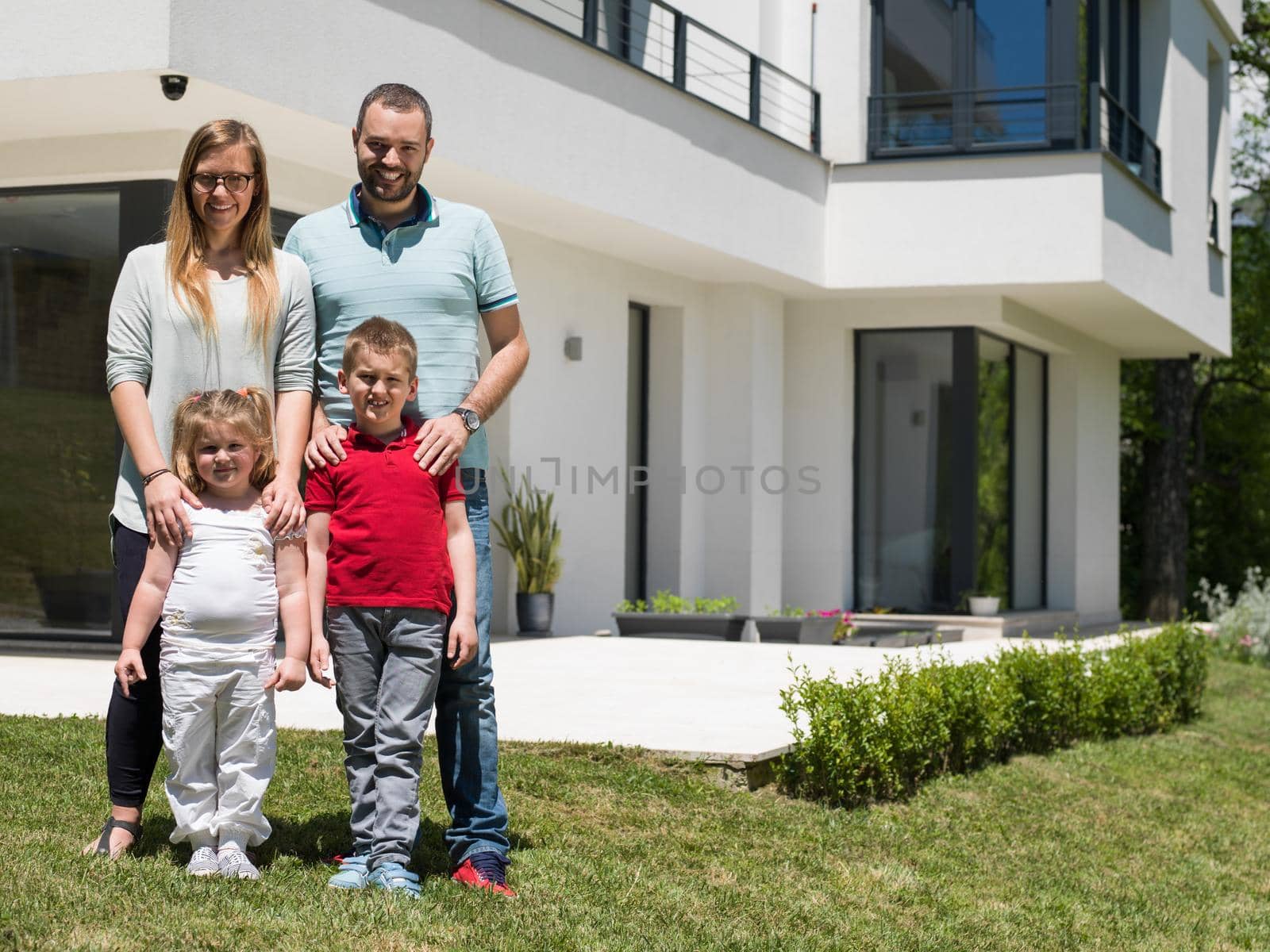 Portrait of young happy family with children in the yard in front of their luxury home of villa