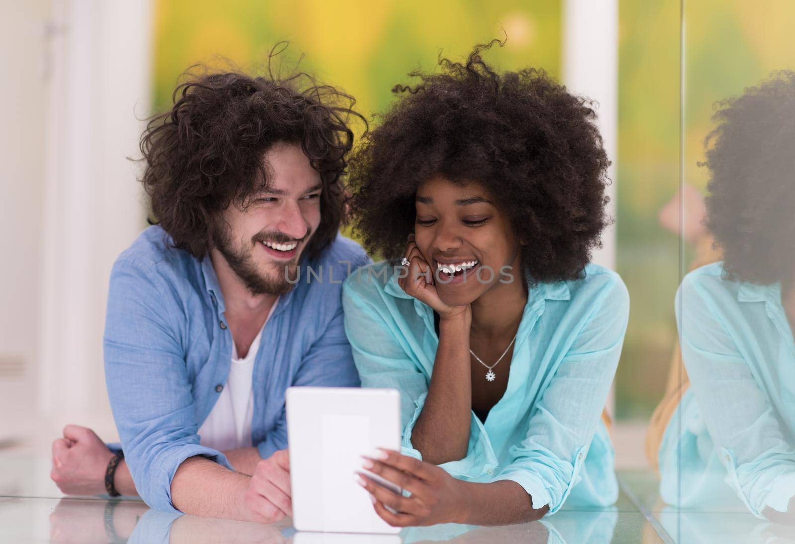 Happy young multiethnic couple lying on floor having fun using Digital Tablet