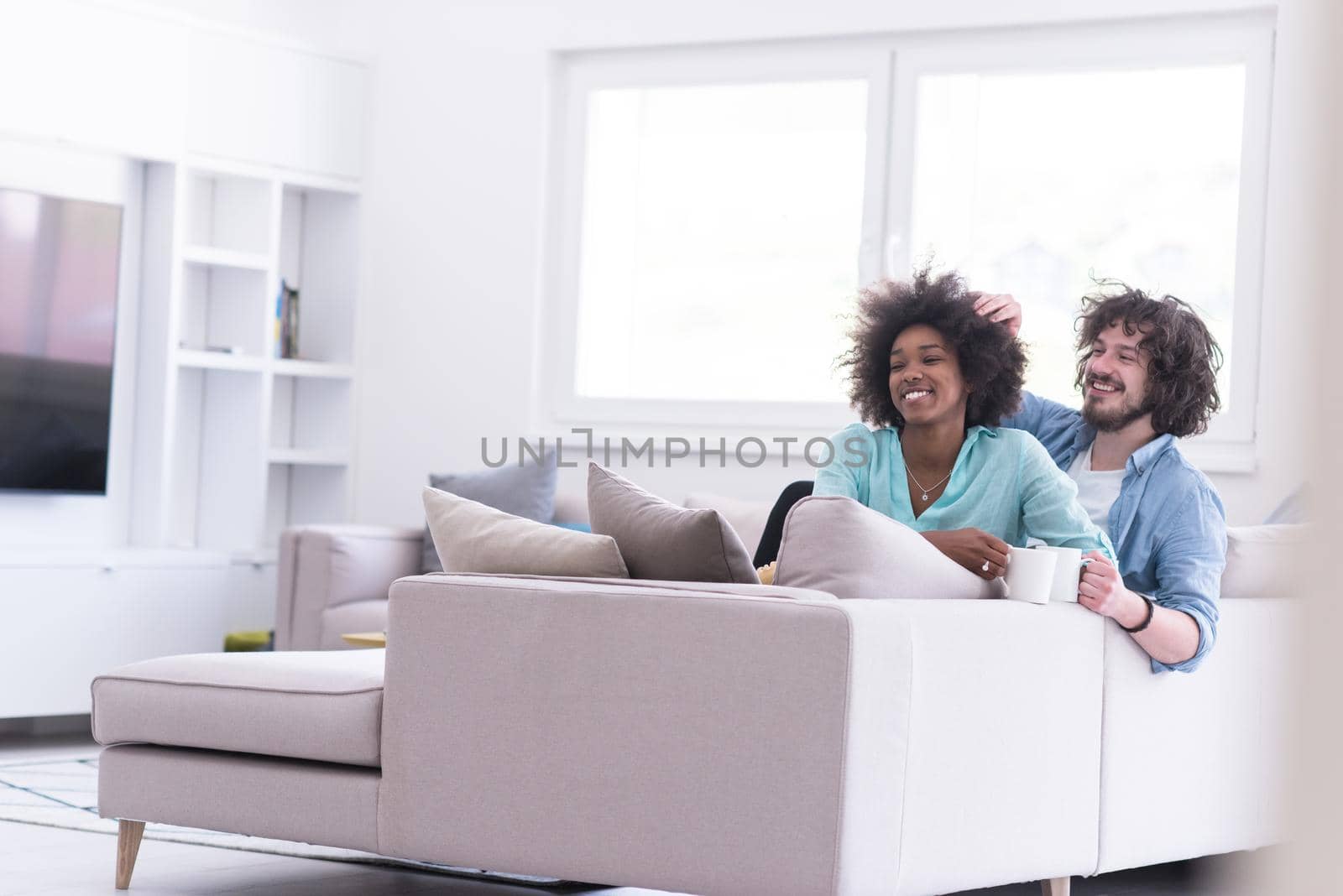 young multiethnic couple sitting on sofa at home drinking coffe, talking, smiling.