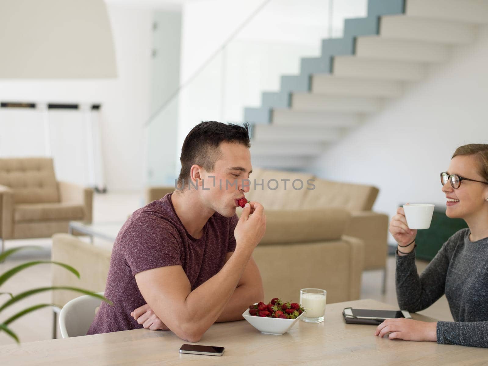 young beautiful handsome couple enjoying morning coffee and strawberries in their luxurious home villa