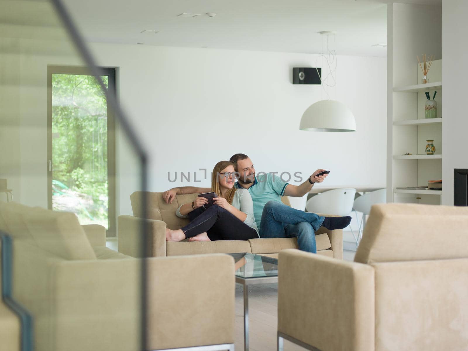 Young couple relaxes on the sofa in the luxury living room, using a tablet and remote control