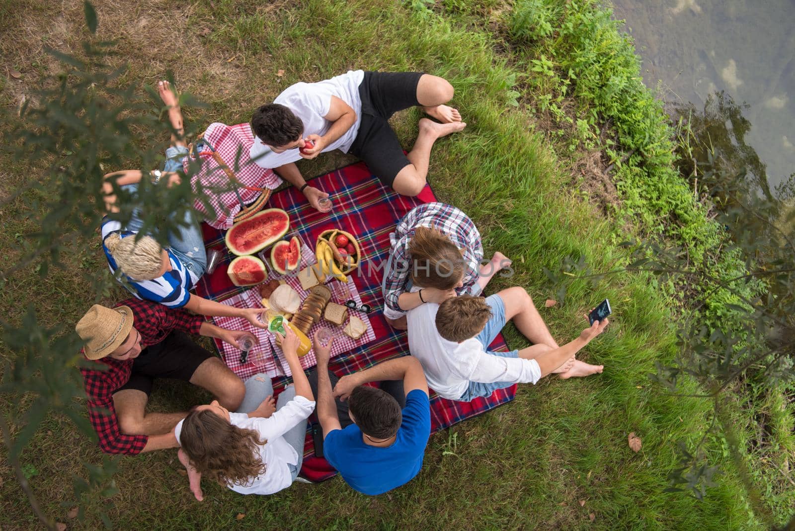 group of young friends enjoying picnic time drink and food in beautiful nature on the river bank top view