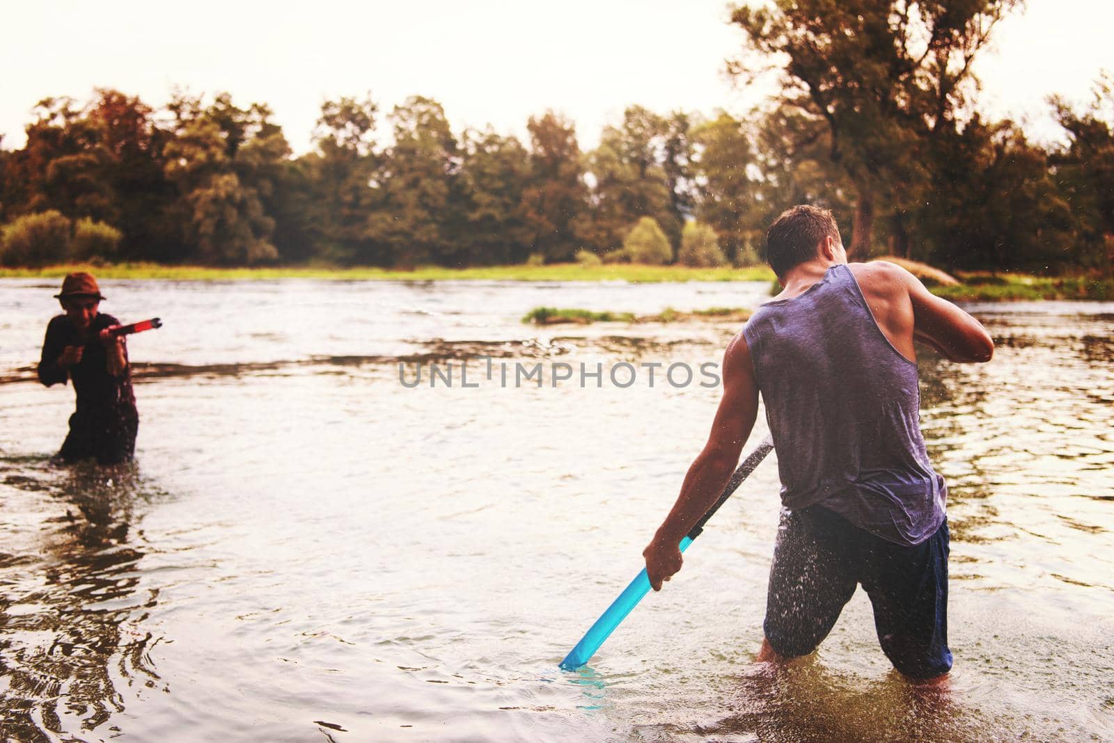 young men having fun with water guns while splashing  each other during sunset on the river