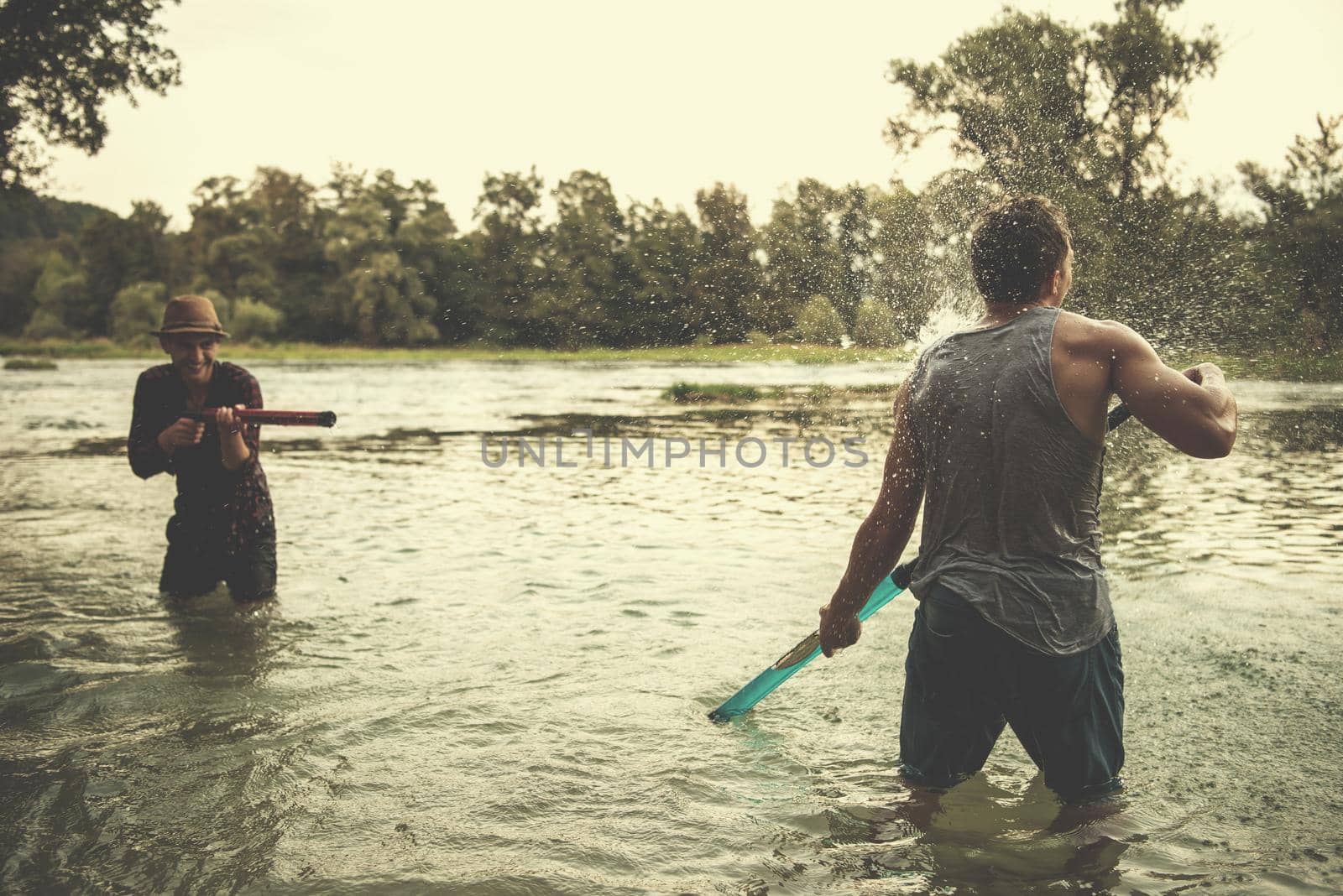 young men having fun with water guns while splashing  each other during sunset on the river