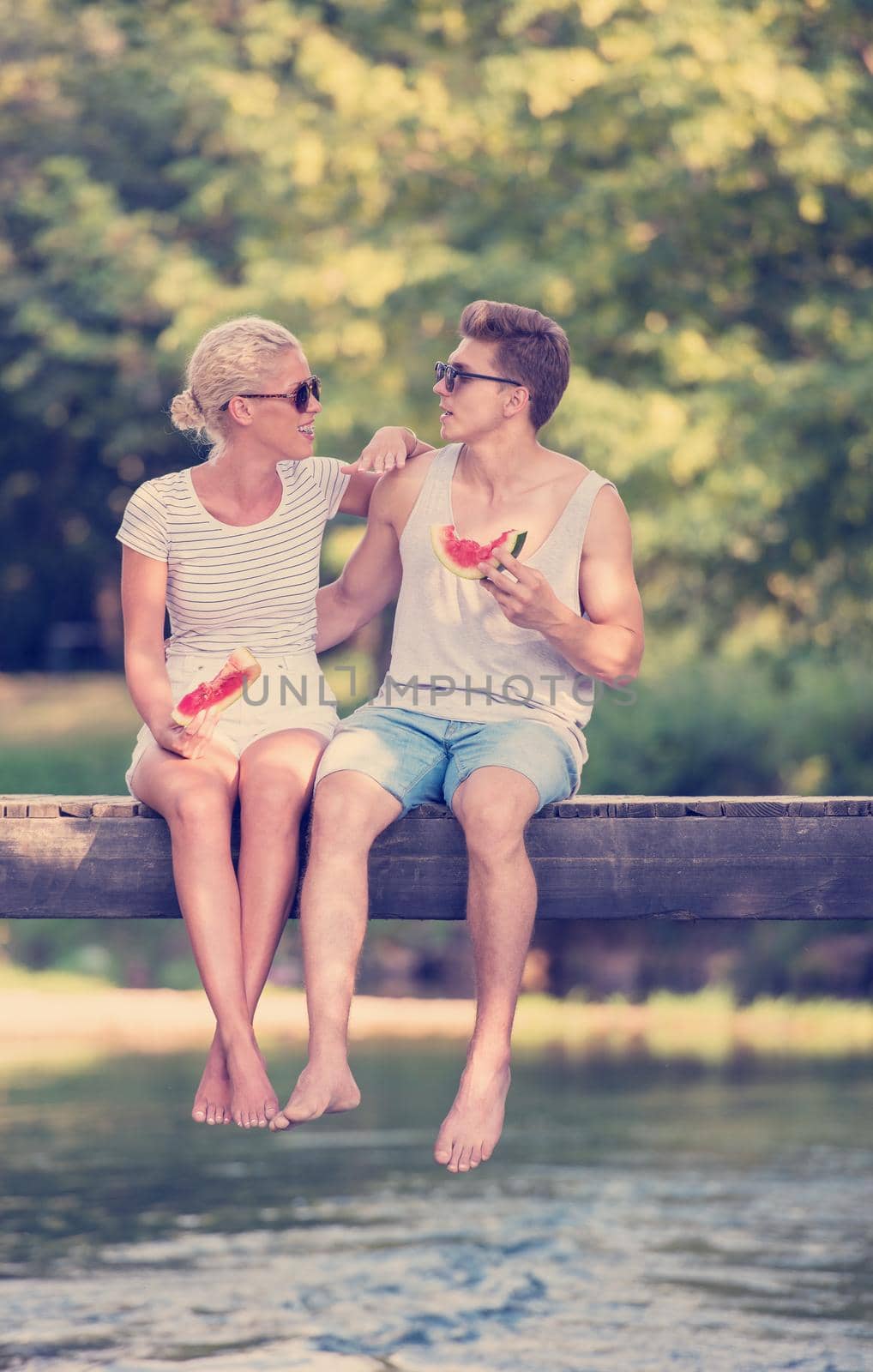 couple in love enjoying watermelon while sitting on the wooden bridge over the river in beautiful nature