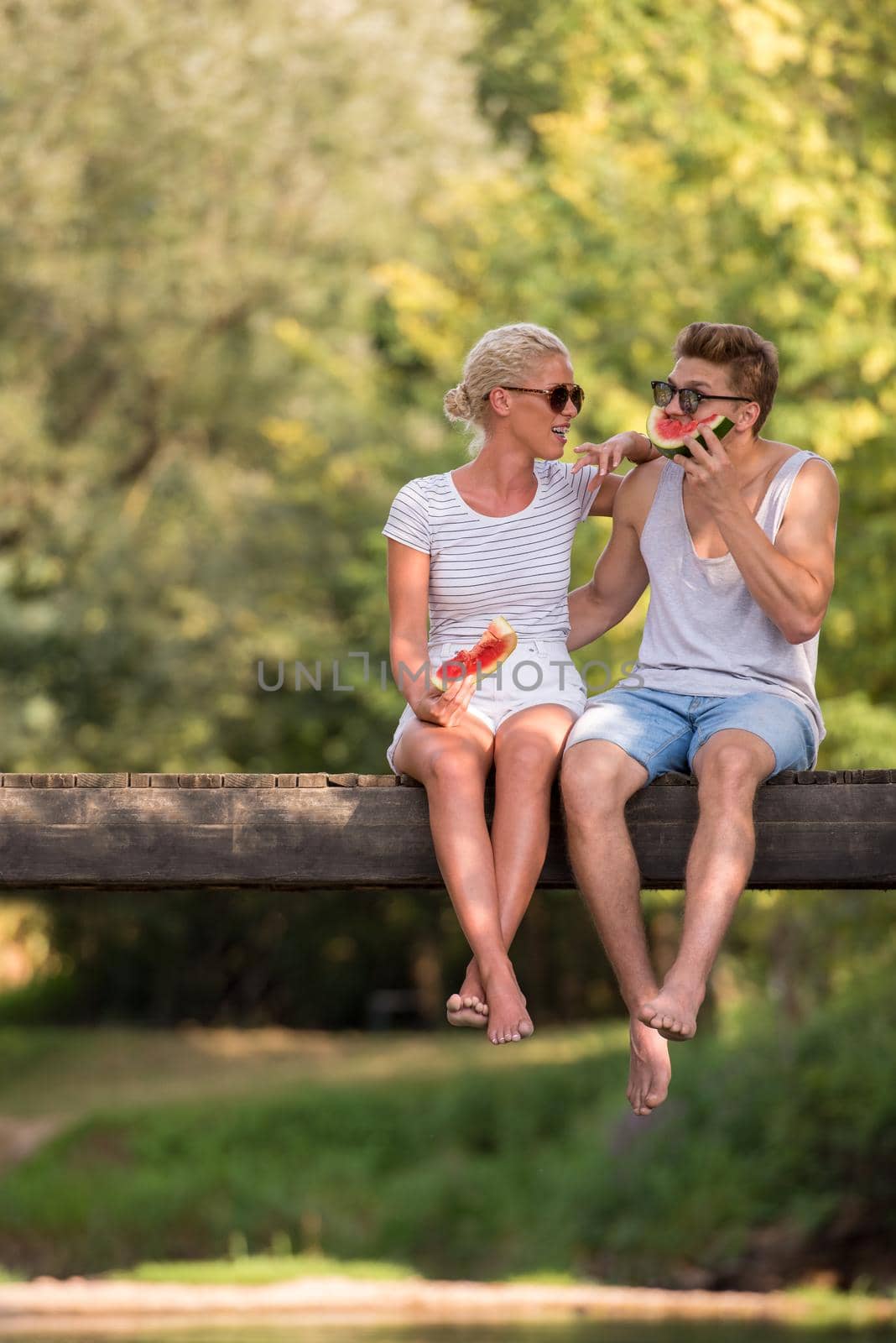 couple enjoying watermelon while sitting on the wooden bridge by dotshock