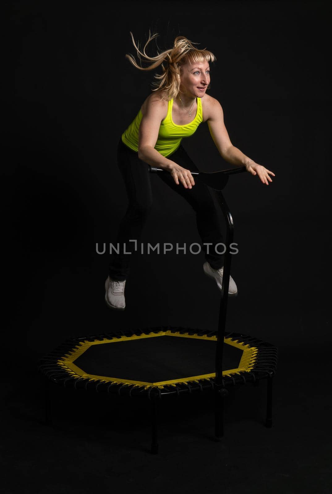Girl on a fitness trampoline on a black background in a yellow t-shirt trampoline fit active body healthy movement, cute club. Person white trainer, physical muscle instructor enjoy by 89167702191