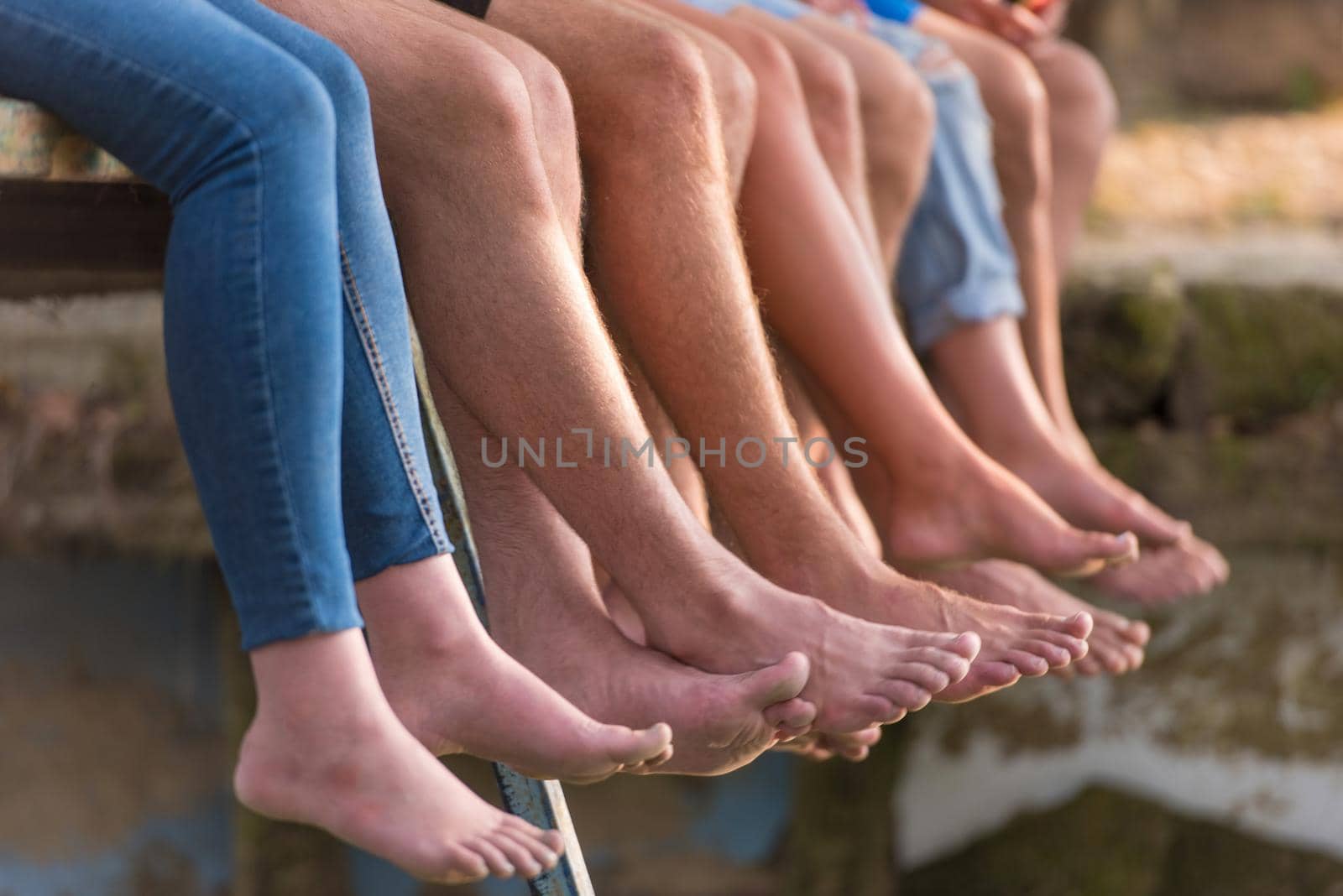 group of  people sitting at wooden bridge over the river with a focus on hanging legs