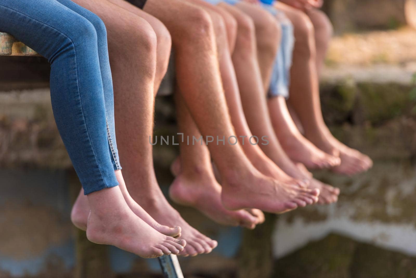 group of  people sitting at wooden bridge over the river with a focus on hanging legs