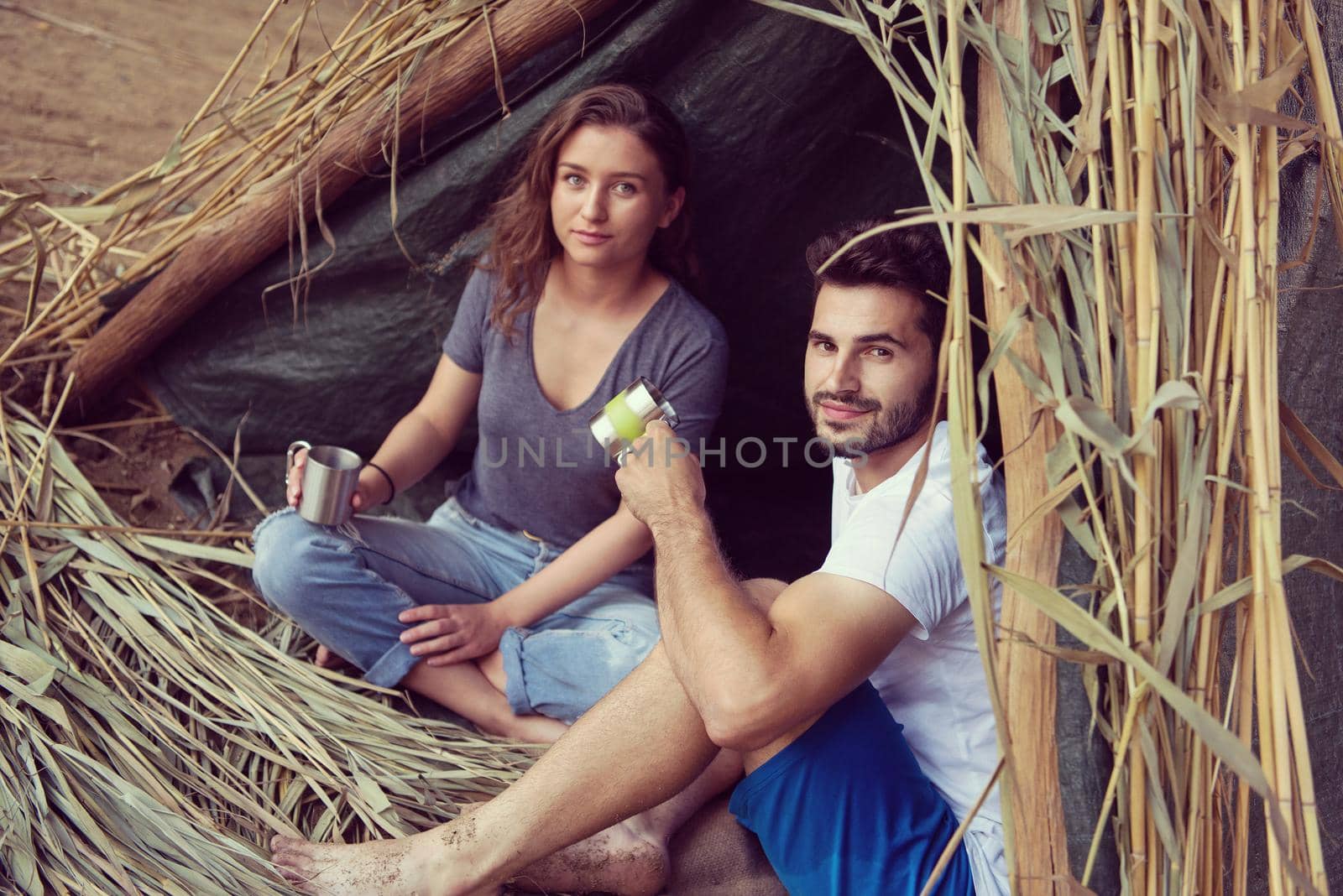 couple in love traveling and spending time together in straw tent while drinking hot tea by the river