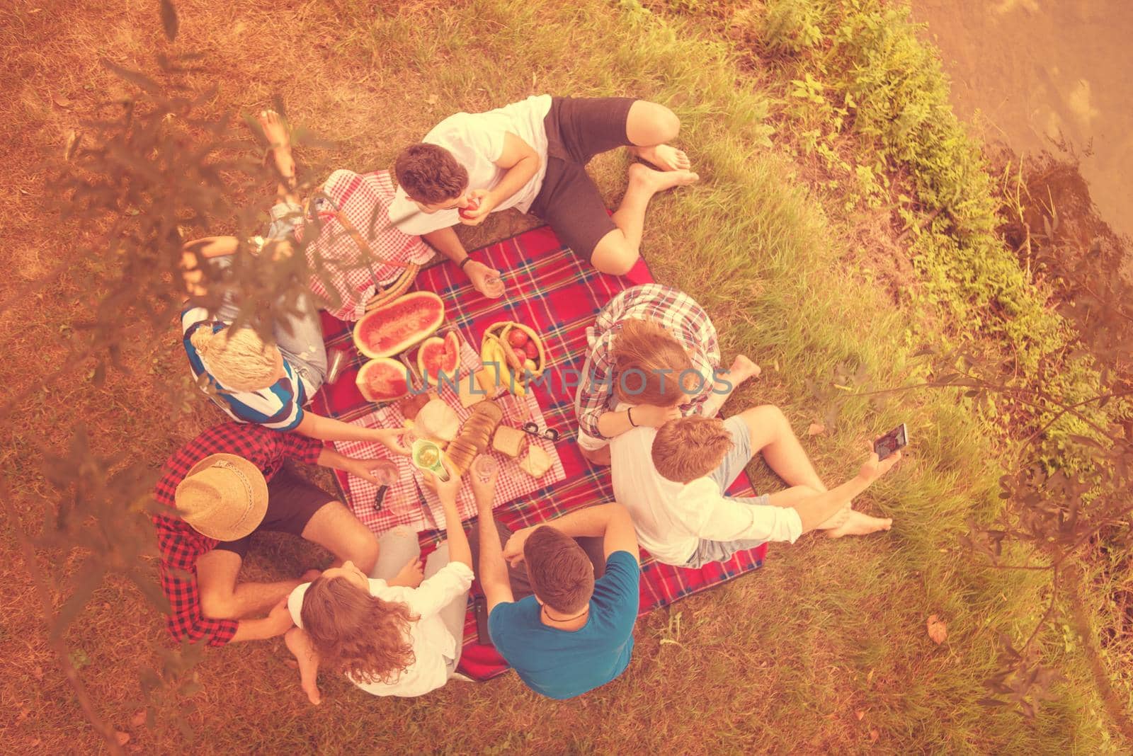 group of young friends enjoying picnic time drink and food in beautiful nature on the river bank top view