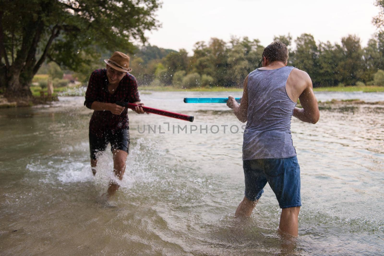 young men having fun with water guns while splashing  each other during sunset on the river