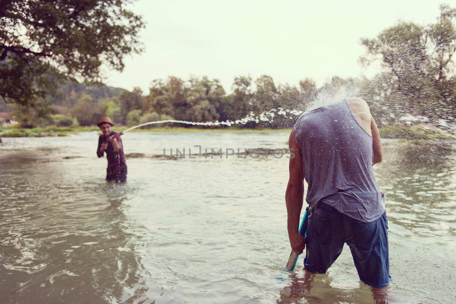 young men having fun with water guns while splashing  each other during sunset on the river