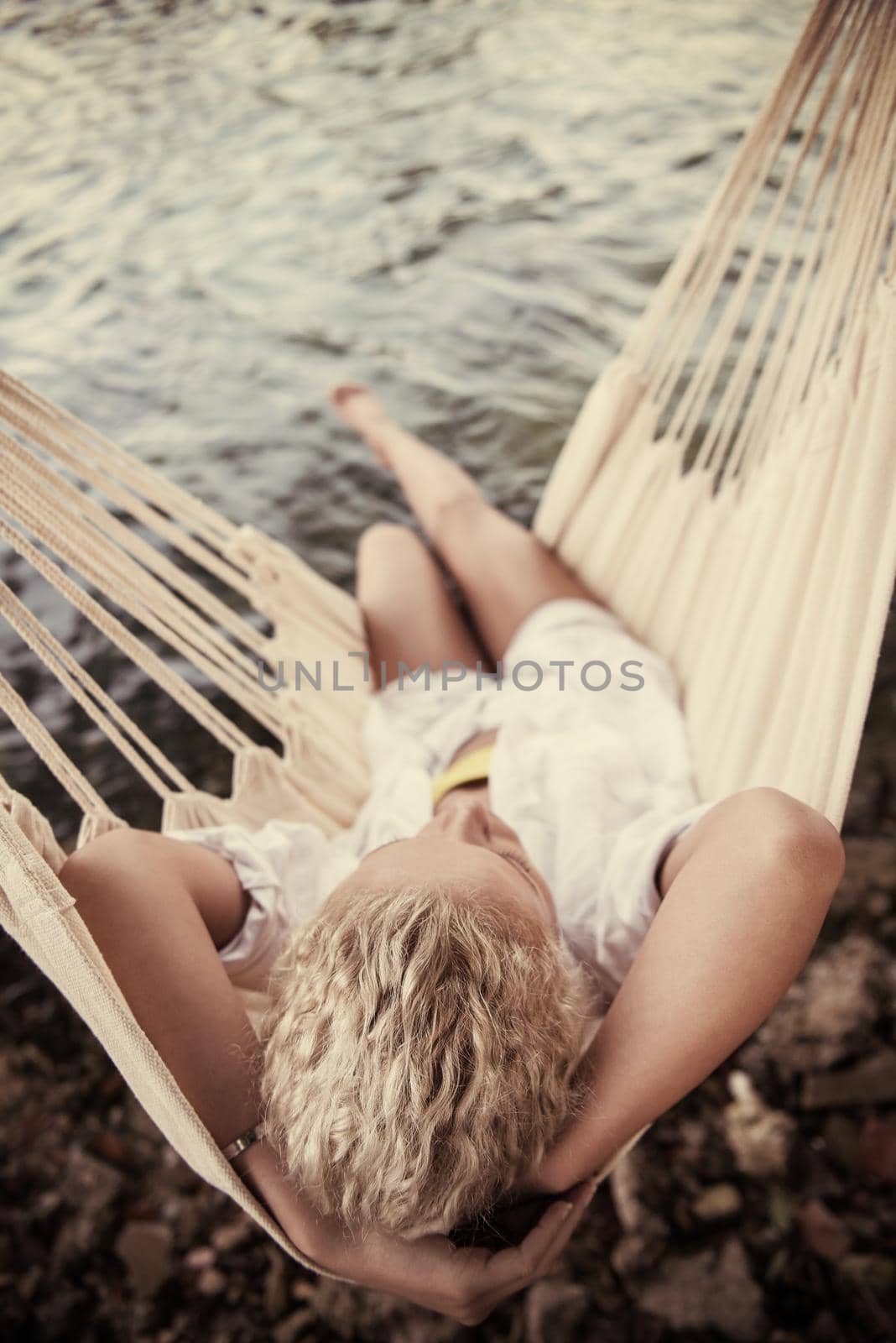Young blonde woman resting on hammock while enjoying nature on the river bank