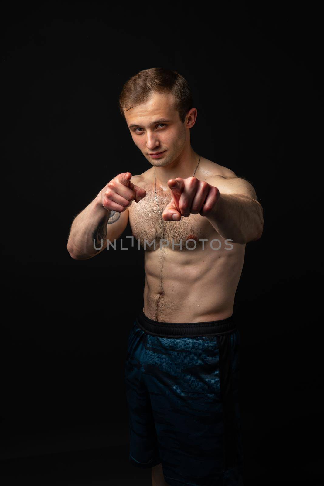 Man on black background keeps dumbbells pumped up in fitness active sexy arm muscular strong athletic dumbbell, person weightlifting. Attractive handsome metal, guy fit fingers point at us