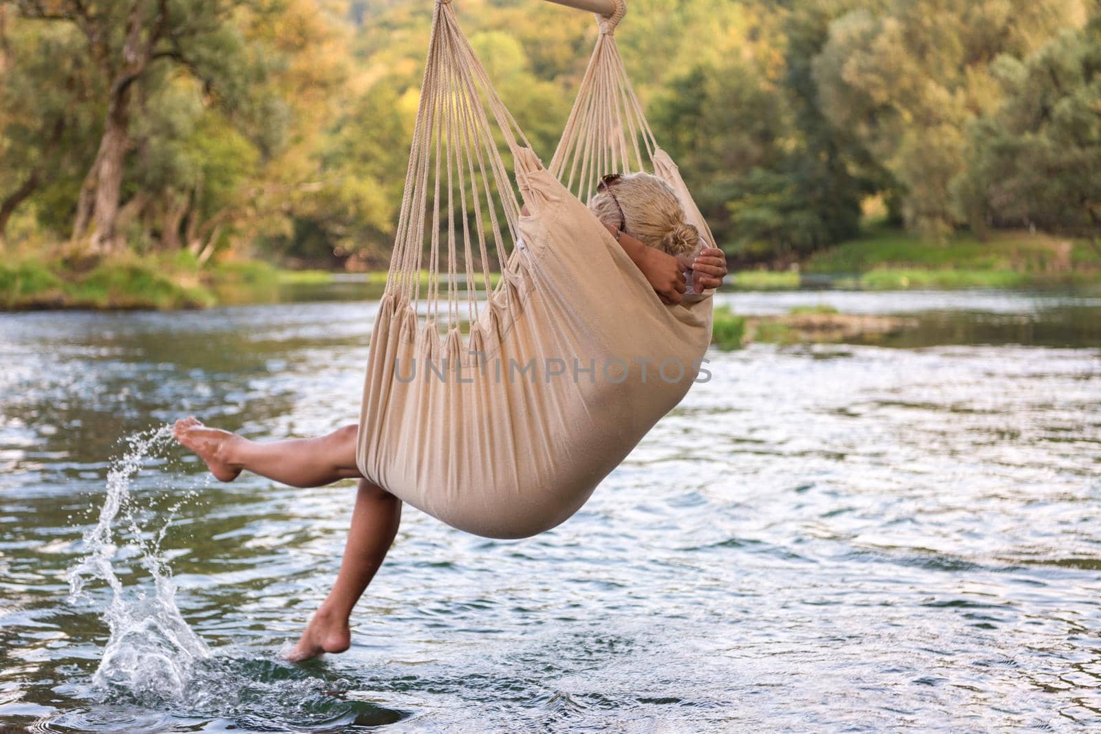 Young blonde woman resting on hammock while enjoying nature on the river bank