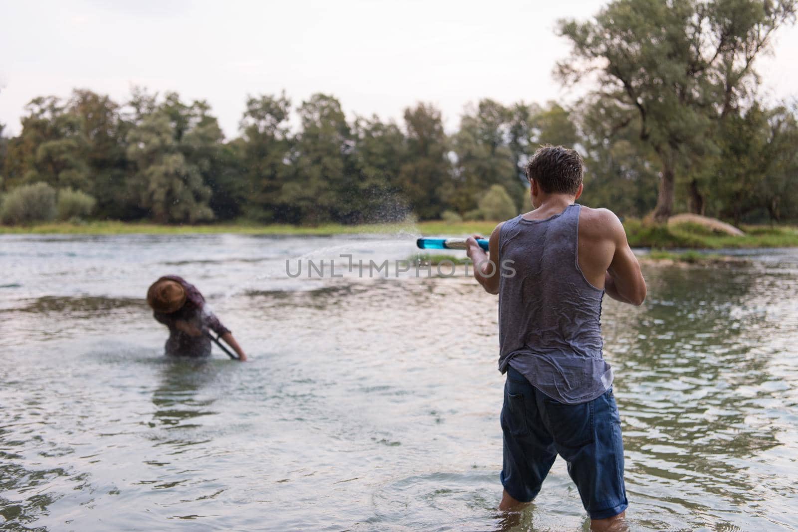 young men having fun with water guns while splashing  each other during sunset on the river