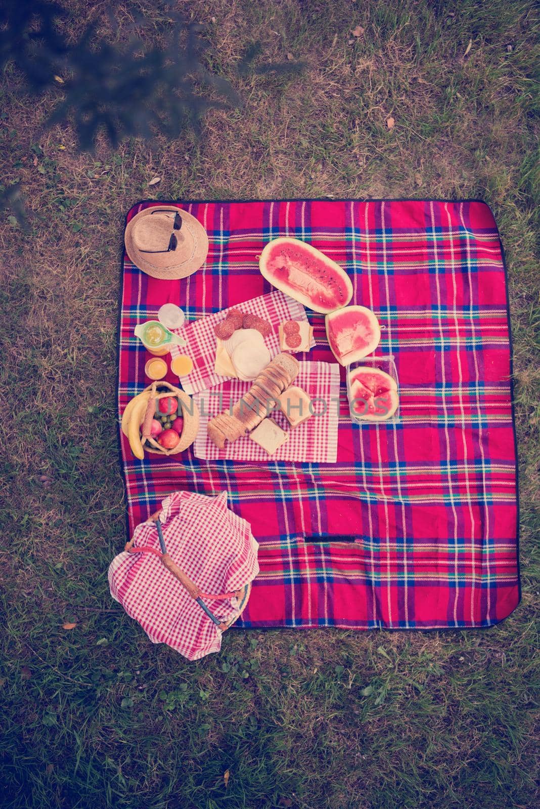 top view of picnic blanket setting on the grass with basket, sandwiches,food and drink