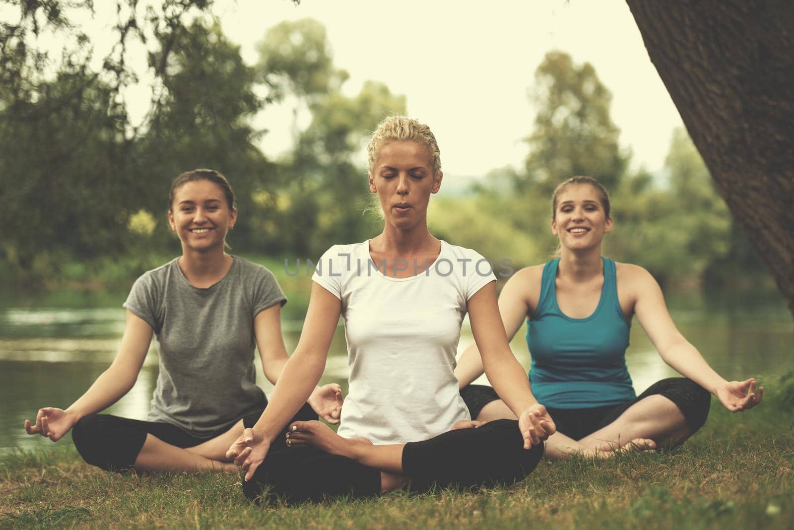 group of young healthy women relaxing while meditating and doing yoga exercise in the beautiful nature on the bank of the river