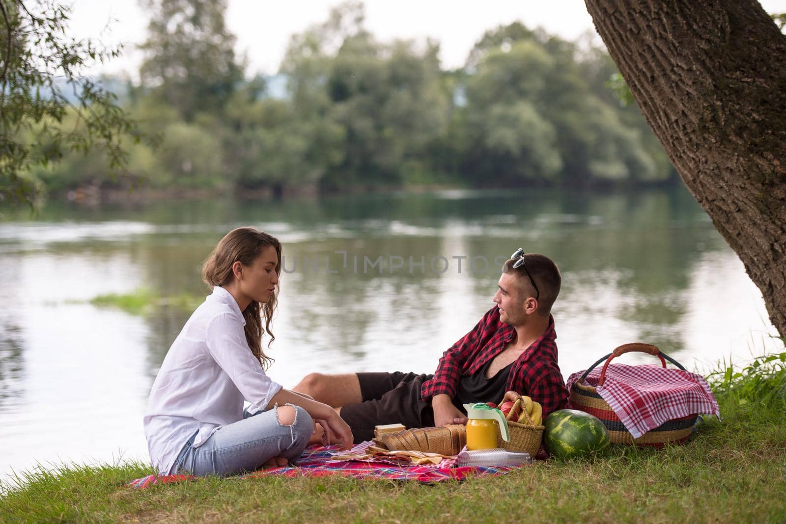 Couple in love enjoying picnic time drink and food in beautiful nature on the river bank