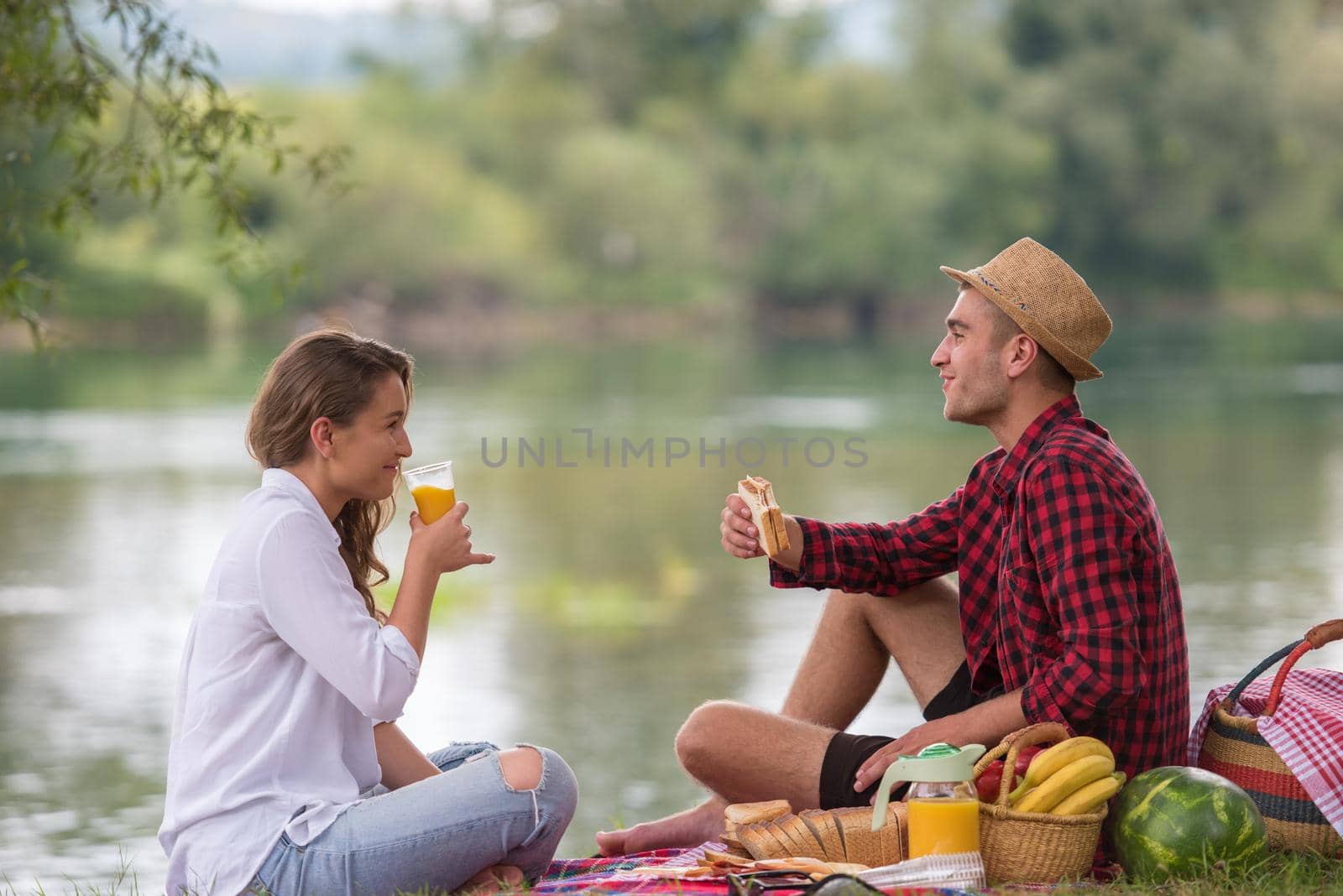 Couple in love enjoying picnic time drink and food in beautiful nature on the river bank