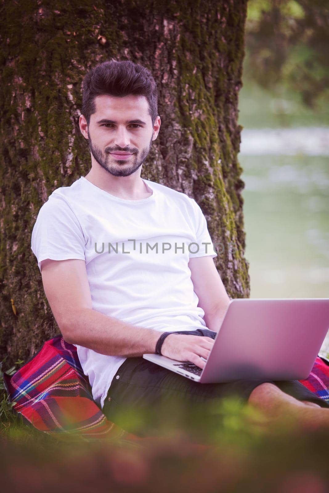man using a laptop computer on the bank of the river by dotshock