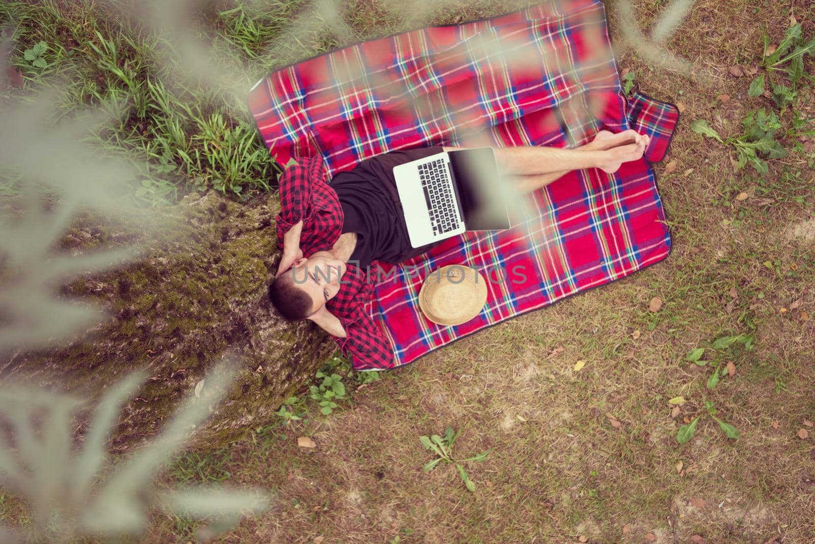 A young freelancer using a laptop computer while working in beautiful nature under the tree top view