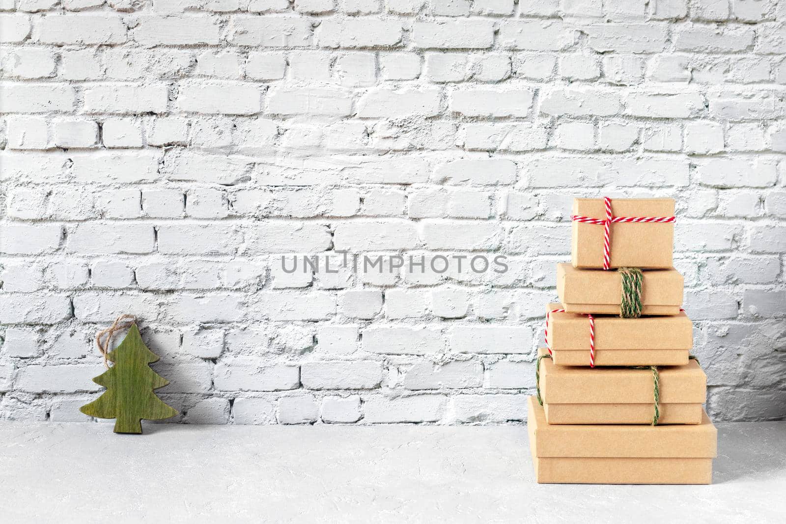 Craft paper gift boxes in a form of New Year tree with a small wooden Christmas tree on brick wall background, minimalism, copy space